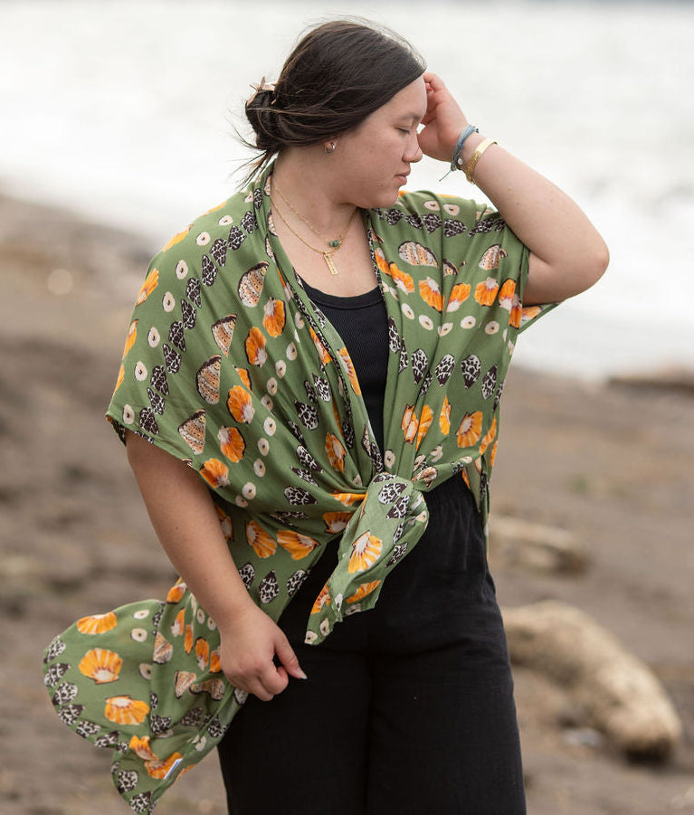 Woman wearing a green patterned shawl on a beach with a blurred landscape in the background
