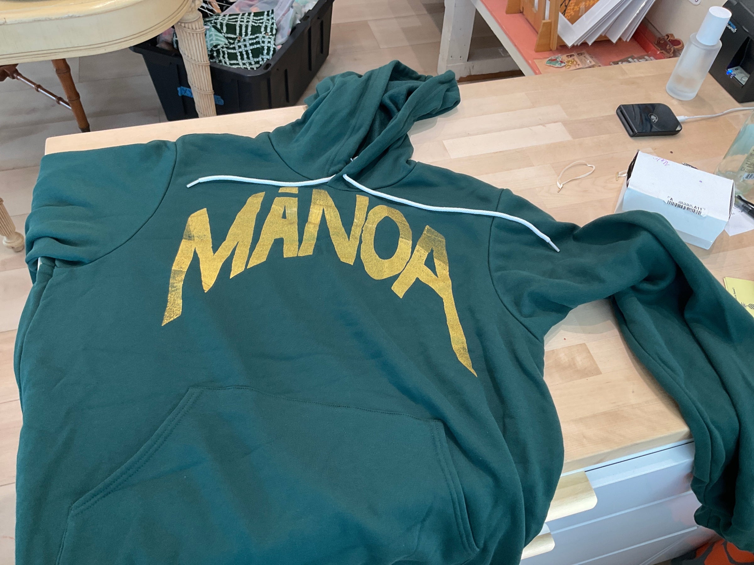 Green sweatshirt with 'Mango' printed in yellow on a wooden surface.
