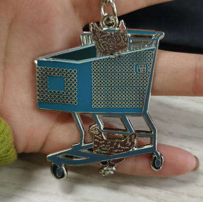 Metallic shopping cart keychain held in a hand on a light surface.