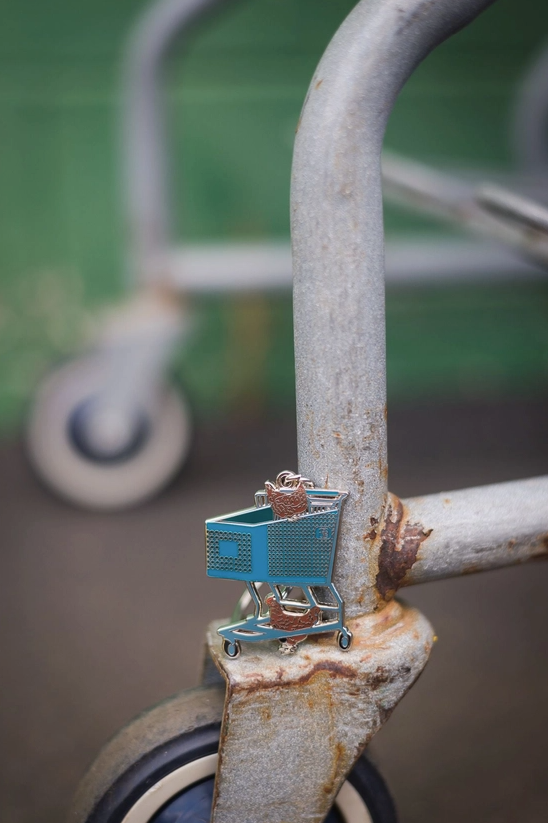 Small blue shopping cart attached to a rusted metal structure with a blurred background