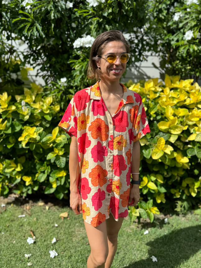 Woman wearing a red floral dress standing outdoors with greenery in the background