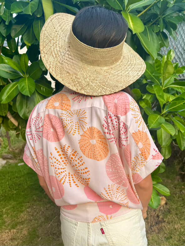 Person wearing a straw hat and a floral shirt in a garden setting