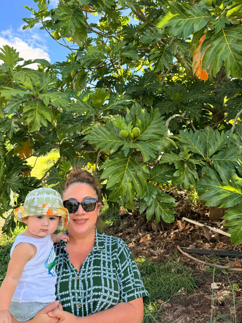 Woman holding a child in front of a large leafy tree