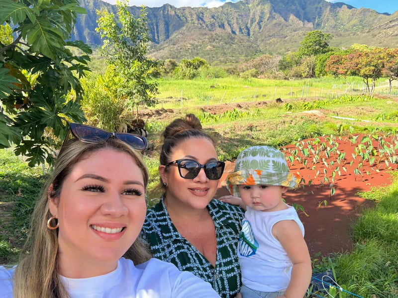 Two women and a child in a scenic outdoor setting with mountains and greenery.