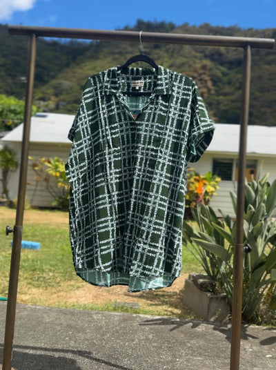 Green and white checkered shirt on a hanger against a natural background with trees and a house.