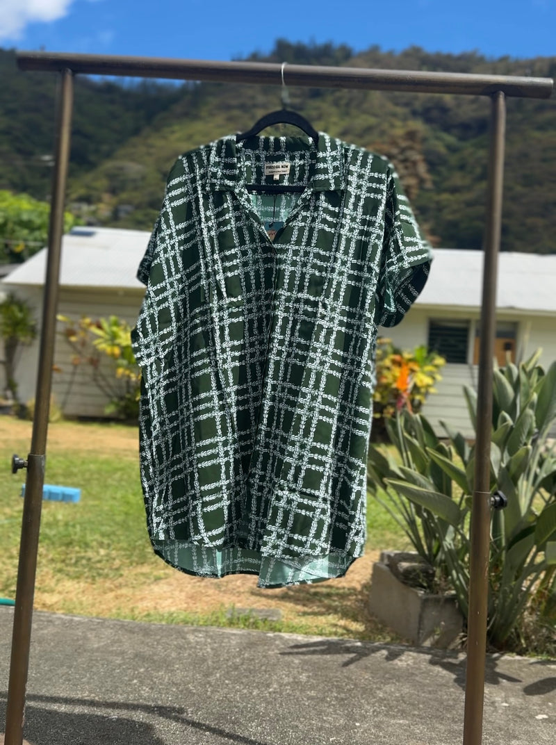 Green and white checkered shirt on a hanger against a natural background with trees and a house.