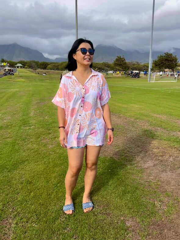 Woman in a colorful dress standing on a grassy field with mountains in the background